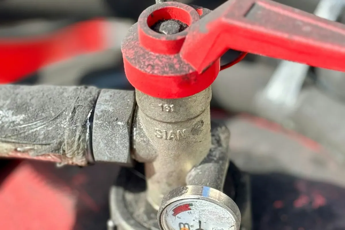 Close-up of a red shut-off valve and pressure gauge on a water line